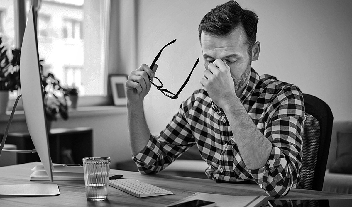 Man rubbing his forehead while sitting at a desk